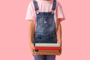 Naklejka premium Little girl with stack of books on pink background