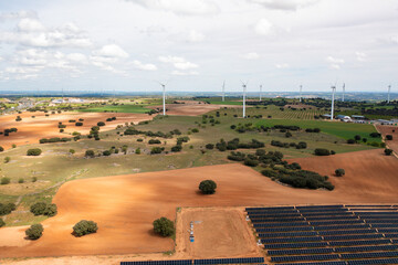 Aerial drone view of sustainable energy landscape with wind turbines and solar panels across farmland producing clean renewable electricity under cloudy sky