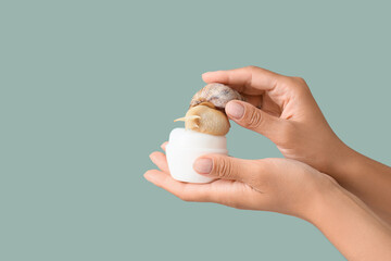 Female hands with snail and jar of cream on green background