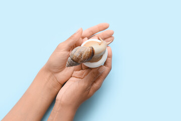 Female hands with snail and jar of cream on blue background