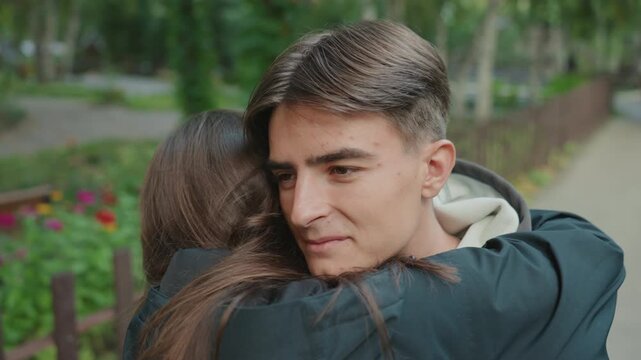 white teen smiling after warm hug near flower beds, bench and pathway backdrop, eyes softening, classmate reconciliation, candid camera, natural sunlight, subtle grin, renewed friendship energy