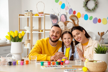 Happy parents with their little daughter painting Easter eggs at table in kitchen