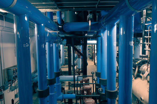 Interior air conditioning chiller room of an commercial or institutional building, large blue pipes in foreground, pumps in background, nobody