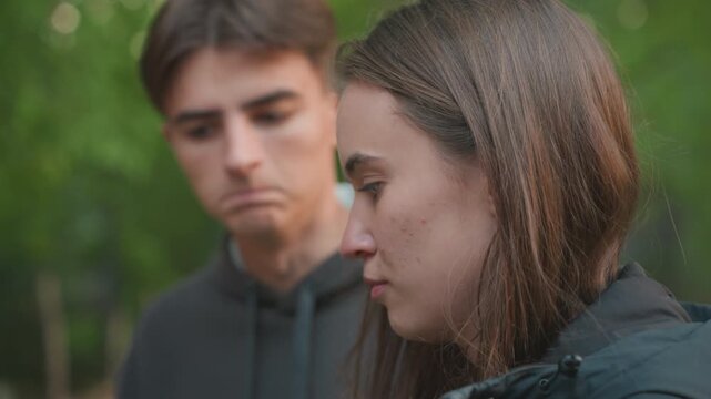 white teenage male listening to friend in park, hoodie and jacket, female closeup with sad expression, empathetic glances and subtle playful reaction from male, candid conversation, natural light,