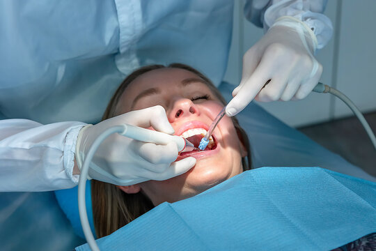 Dentist performing professional dental cleaning using an ultrasonic scaler. Preventive oral hygiene procedure focused on plaque removal and maintaining healthy teeth.