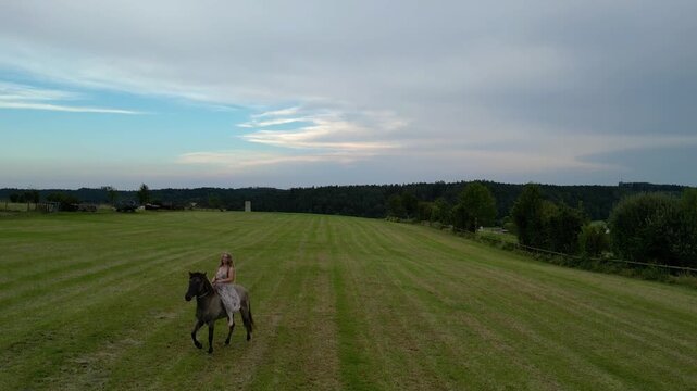 Drone perspective of a woman riding bareback and guiding her rearing horse using a neck ring in open countryside