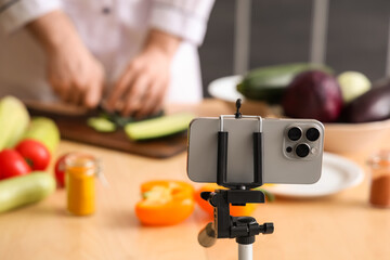 Male chef with fresh vegetables recording cooking video on mobile phone in kitchen