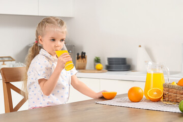 Cute little girl drinking orange juice in kitchen