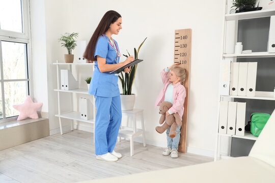 Female pediatrician measuring height of little girl in clinic