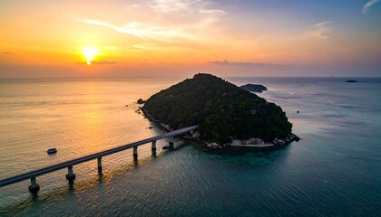 Aerial view of a bridge connecting two islands during a sunset. Calm sea reflects golden sunlight. A small boat is visible