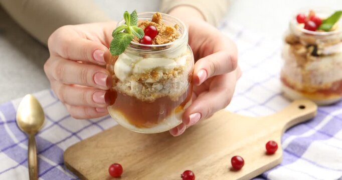 Woman with tasty trifle dessert in glass jar at table, closeup