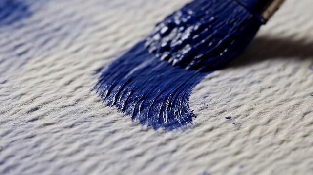 Close-up of a paintbrush applying vibrant blue paint to a textured white surface, creating an artistic stroke.