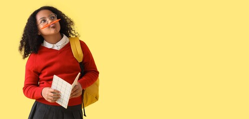 Funny thoughtful African-American schoolgirl with notebook on yellow background with space for text
