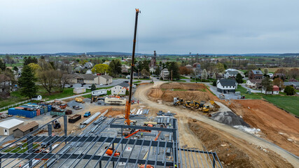 A building is under construction in a rural area. Cranes and machinery are present on site. Nearby...