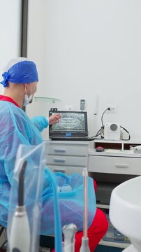 Vertical video of a professional male dentist in a blue surgical gown holding up a dental radiograph.