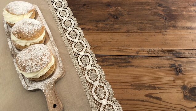 Three Swedish semla buns with powdered sugar on rustic board &ndash; traditional pastry for Fettisdagen (Fat Tuesday) with copy space