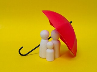 Wooden family figures under a umbrella on a blue background. Insurance coverage and protection concept.