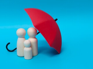 Wooden family figures under a umbrella on a blue background. Insurance coverage and protection concept.
