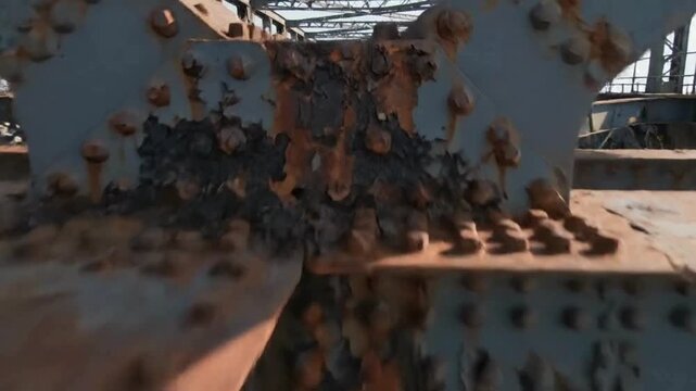Close up drone fly through dynamic movement along severely corroded rusty steel truss bridge structure showing heavy industrial decay and deterioration over river water