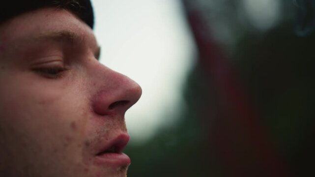 white man lighting cigarette with hands, closeup fingers sparking lighter, ember glow on cigarette tip, lips drawing smoke and inhaling, tactile ritual captured in shallow depth, roadside pause