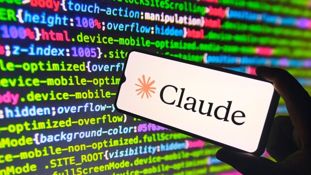 Hand holding smartphone with Claude logo on screen in front of coding background