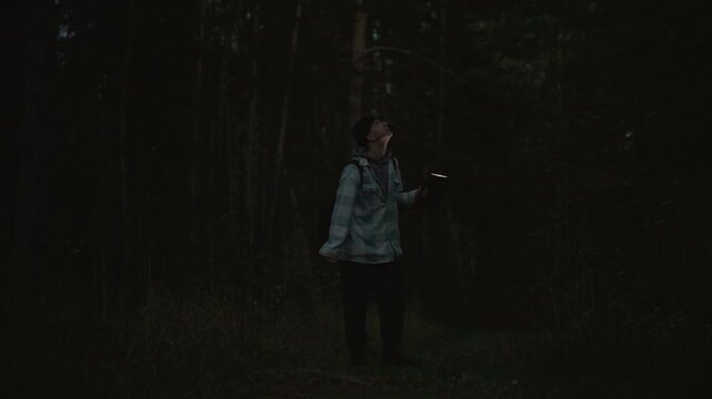 night hiker in pine forest flashlight guiding through firefly glow. Solitary outdoor explorer walks along narrow trail into dark woods, backpack slung, discovering bioluminescent lights