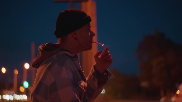 night street portrait white man vaping, quiet bus stop under amber lamps, contemplative drifter exhales visible smoke, hoodie and beanie silhouette, cinematic bokeh, urban solitude mood