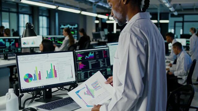 A professional office setting with a focus on data analysis. Over-the-shoulder angle captures screens with charts, resembling a video scene.