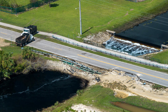 Construction trucks blocking road access at destroyed bridge after hurricane flooding in Florida. Equipment at roadwork site. Reconstruction of damaged road after flood water washed away asphalt