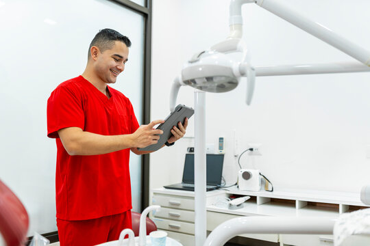 Male dentist wearing red scrubs consulting digital tablet