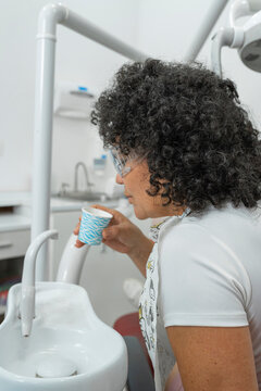 Vertical shot of a female patient rinsing her mouth with a cup in a dental office