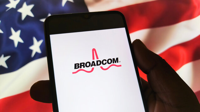 Hand holding smartphone with Broadcom logo on screen in front of American flag