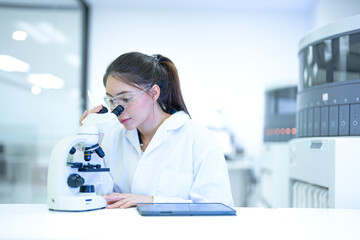 Focused female scientist using a microscope and digital tablet to analyze research data in a modern sterile laboratory. Professional medical researcher working on disease diagnosis projects.