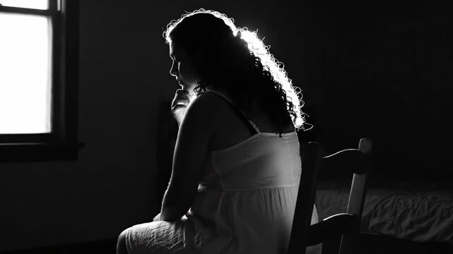 Isolated chubby teen sits reflecting on her personal prison, captured in dramatic monochrome backlighting.