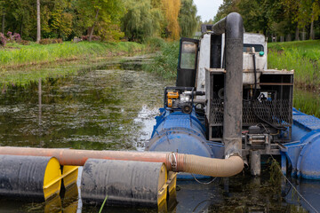 Water cleaning boat works on a canal during a sunny day in an urban park with trees and greenery