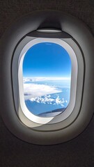 Airplane window view of fluffy white clouds meeting bright blue sky and distant ocean horizon