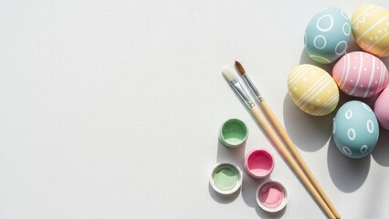 Colorful easter egg painting supplies including painted eggs, brushes, and paint pots arranged on a white canvas background with ample copy space for text