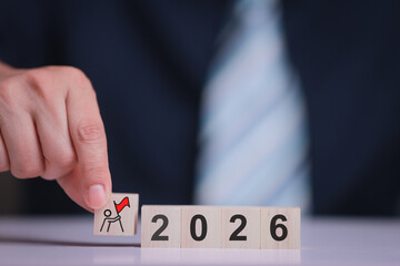 Businessman hand arranging wooden block with flag and number 2026 showing determined business goal success concept for future corporate