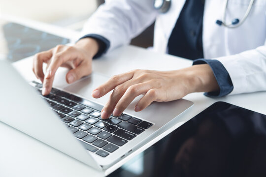 Close up, female doctor hands working on laptop computer at doctor's office with digital tablet on table in hospital or medical clinic. - Powered by Adobe