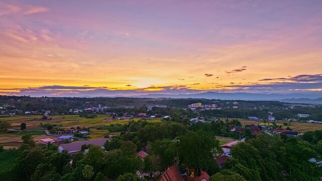 A breathtaking aerial view of a lush green valley surrounded by rural village. A winding river cuts through the serene landscape under a clear, expansive sky, creating a sense of natural beauty