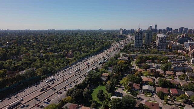 Drone dolly to major 401 highway cutting through residential neighborhoods, road divides forest from apartment buildings