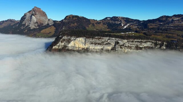 Breathtaking aerial view of a dramatic rocky cliff edge standing above a sea of clouds in the Stoos region of Switzerland.