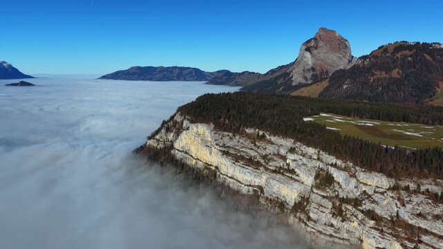 Drone flying alongside a steep alpine ridge (Fronalpstock style) with a massive cloud inversion covering the landscape below.