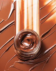 Rich creamy chocolate spread sits within a small glass jar surrounded by textural swipes