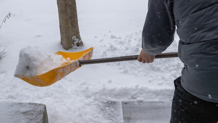 Snow shoveling in winter landscape, individual using yellow shovel to clear snow from walkway, showcasing winter maintenance and outdoor activity © JuliaDorian