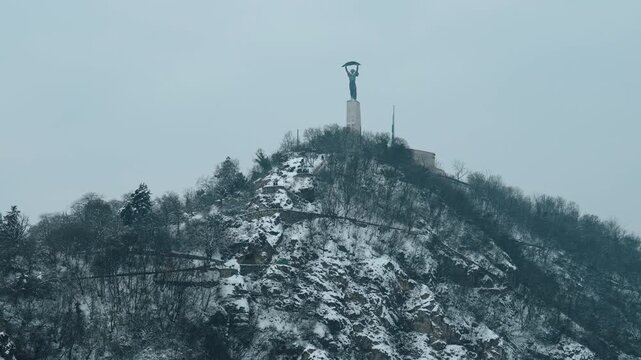 Winter view of the Monument for Daniel Bogdanich in Budapest, Hungary. The scene shows the statue in cold weather conditions with cloudy weather, a seasonal atmosphere, and the statue on a hill.