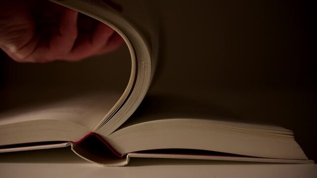 Close-up of an open book as a page is turned slowly, forming a curved shape in soft light. Calm and timeless reading and storytelling atmosphere