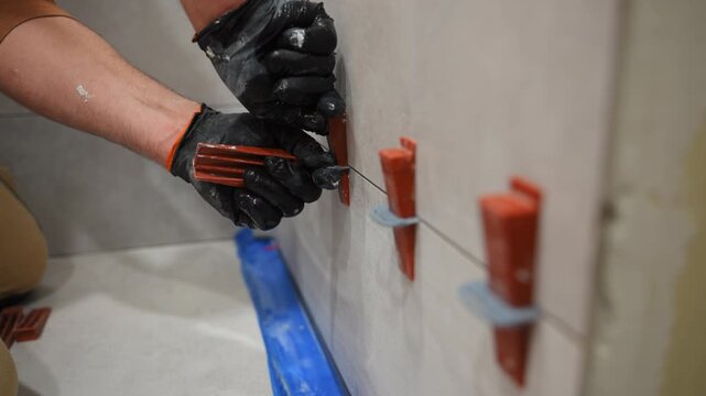 POV construction worker wearing protective gloves installing tile spacers on a wall using pliers. precise tile alignment, renovation work, installation techniques.