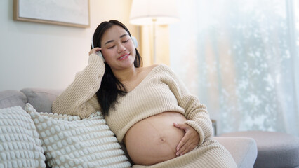 Pregnant woman relaxing on a sofa while listening to music with headphones. Pregnancy wellness and maternal health concept.