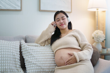 Pregnant woman relaxing on a sofa while listening to music with headphones. Pregnancy wellness and maternal health concept.